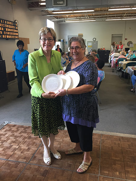 Two Rose Centers participants holding up paper plates explaining why Rose Center meals matter to them for the hashtag SaveLunch campaign