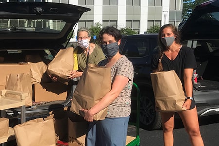 Three volunteers loading a van with bags of groceries for delivery