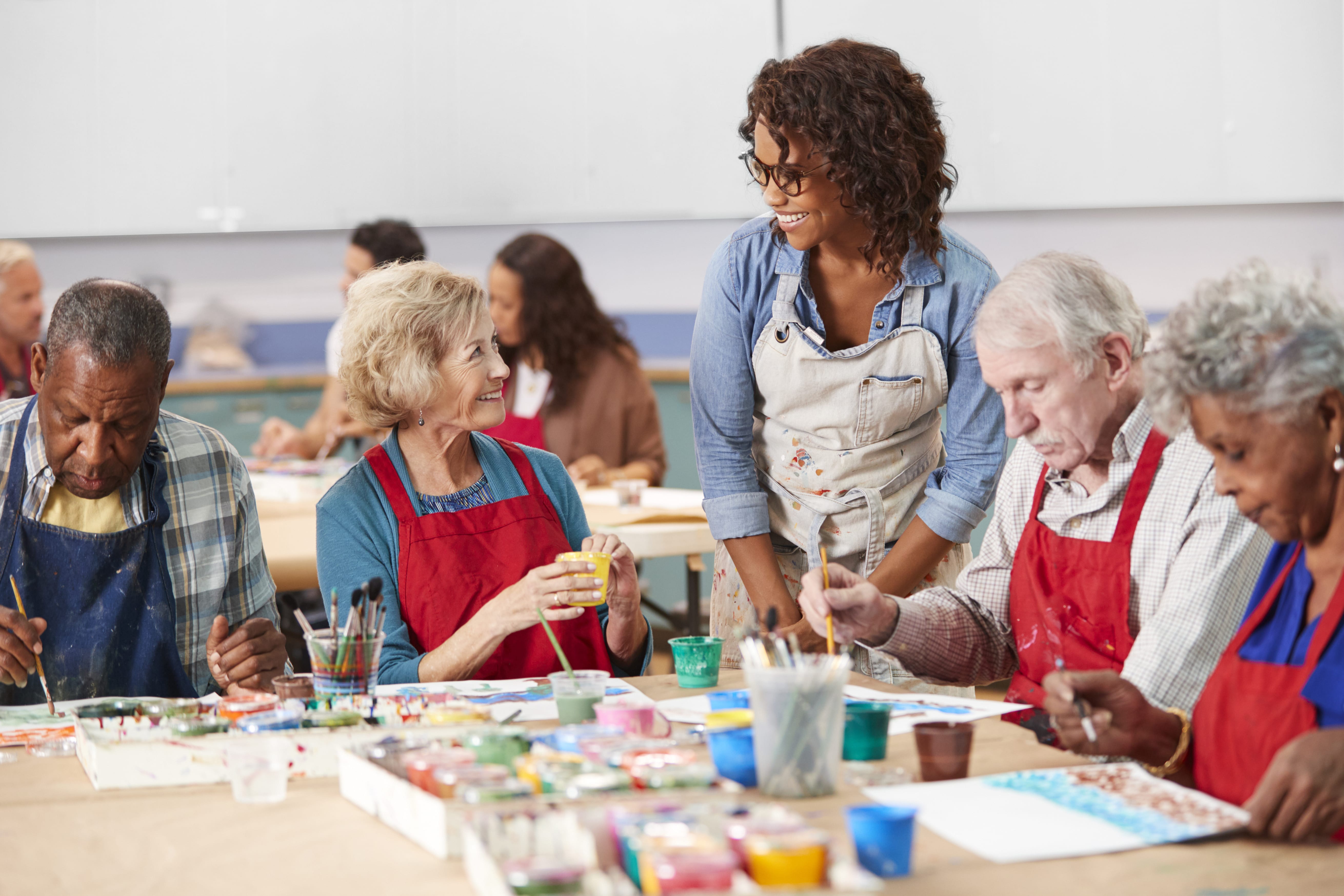 A volunteer helping a table of older adults with a painting project