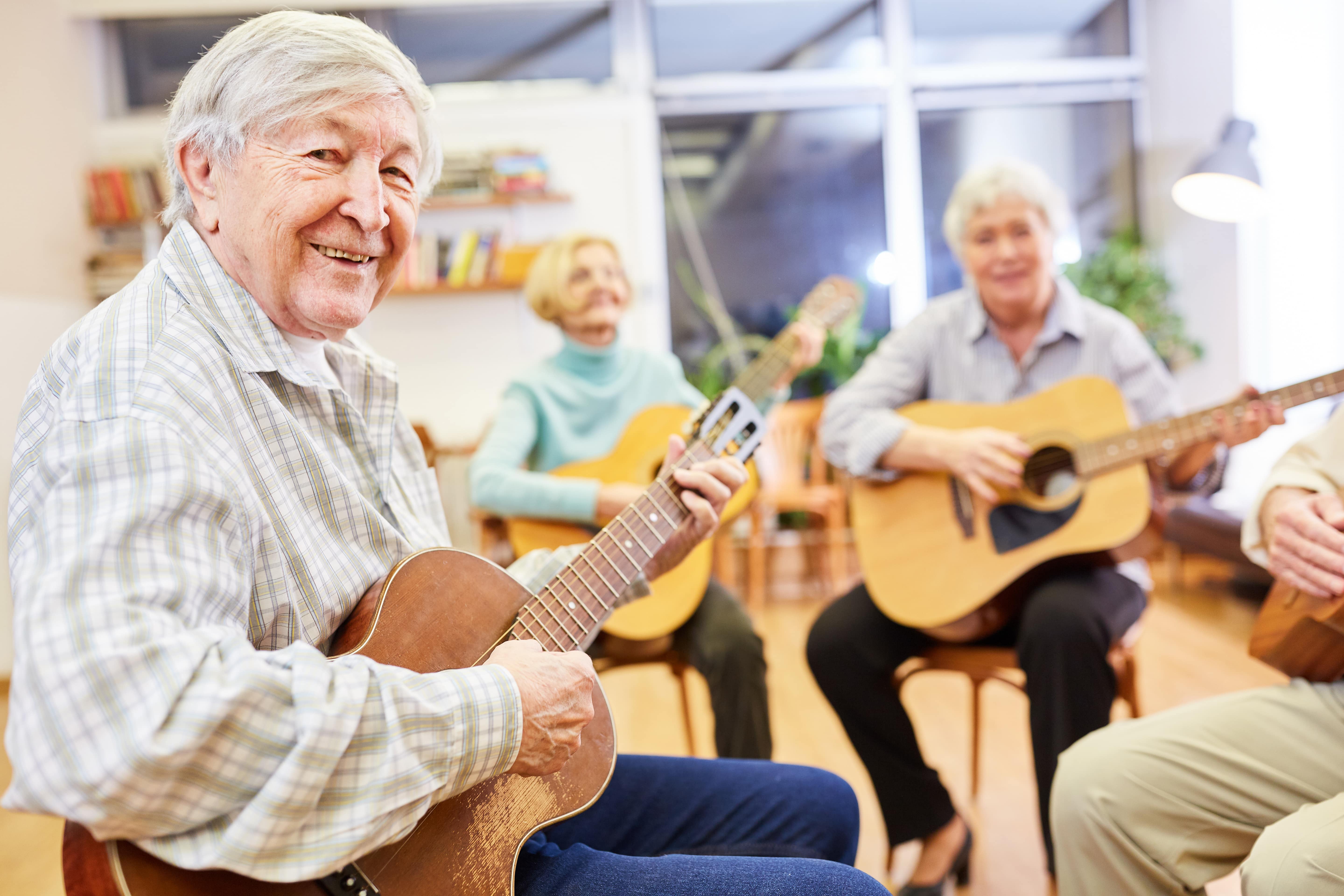 An older adult playing the guitar at a group music session
