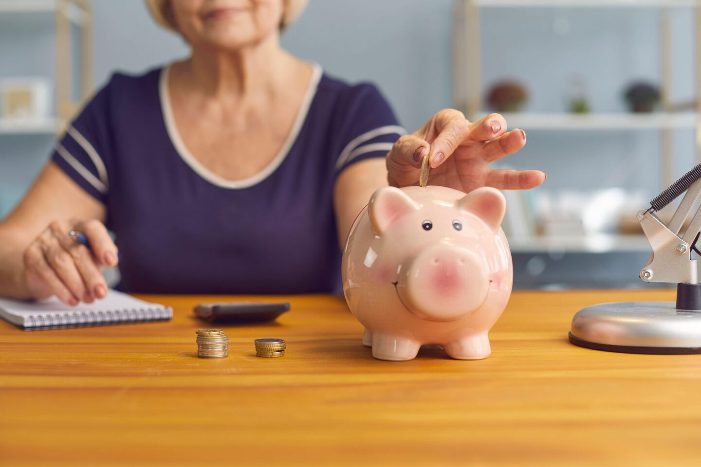 An older woman adding money to a piggy bank