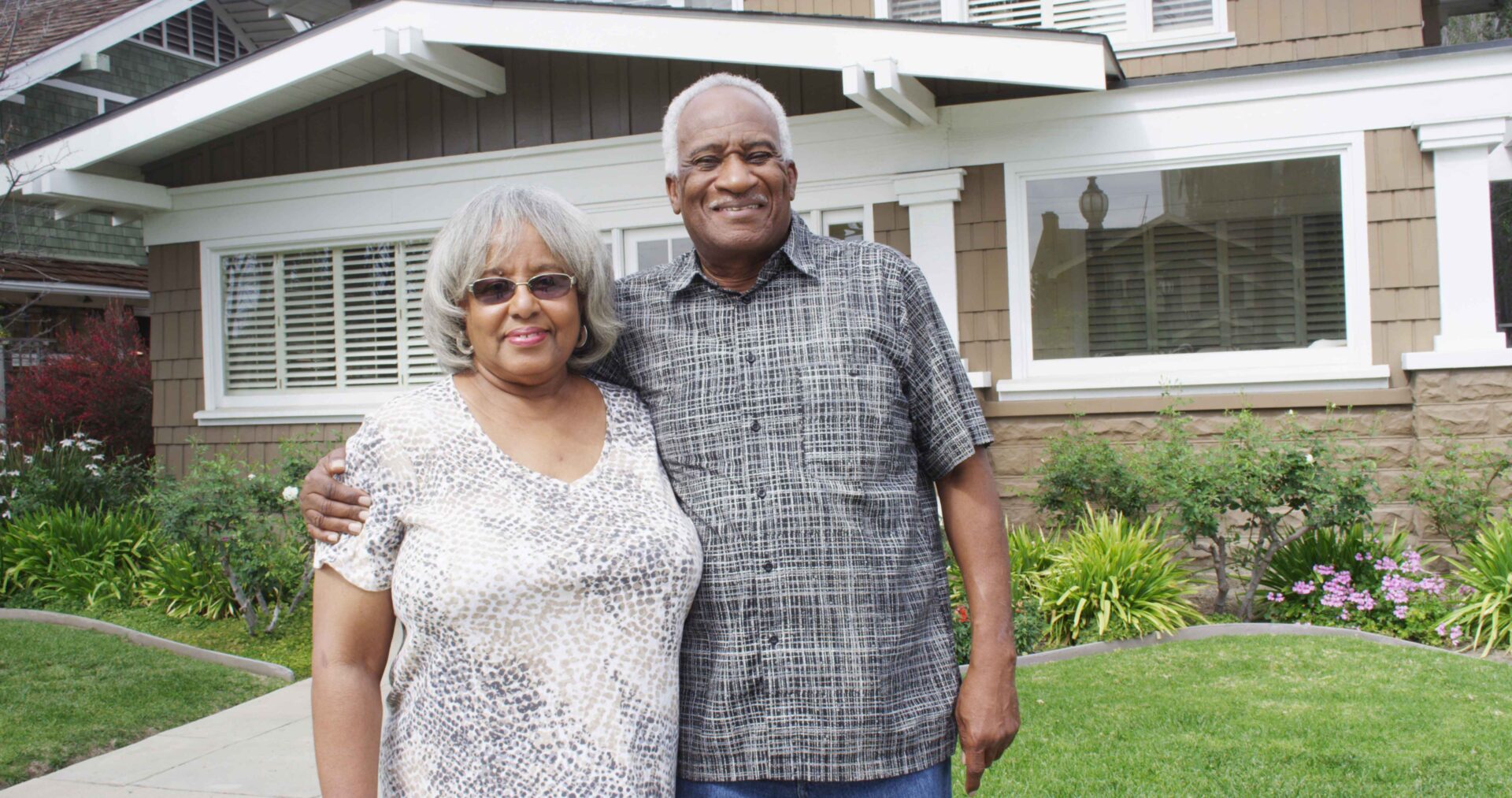 An older couple embracing in front of their home